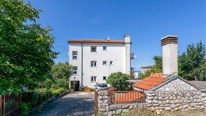 A multi-story building with a red-tiled roof, a stone wall, and a paved driveway. - Beach front apartment in Crikvenica (Crikvenica)