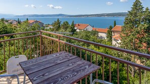 A balcony with a wooden table and metal chairs, overlooking a lake with houses and trees. - Beach front apartment in Crikvenica (Crikvenica)