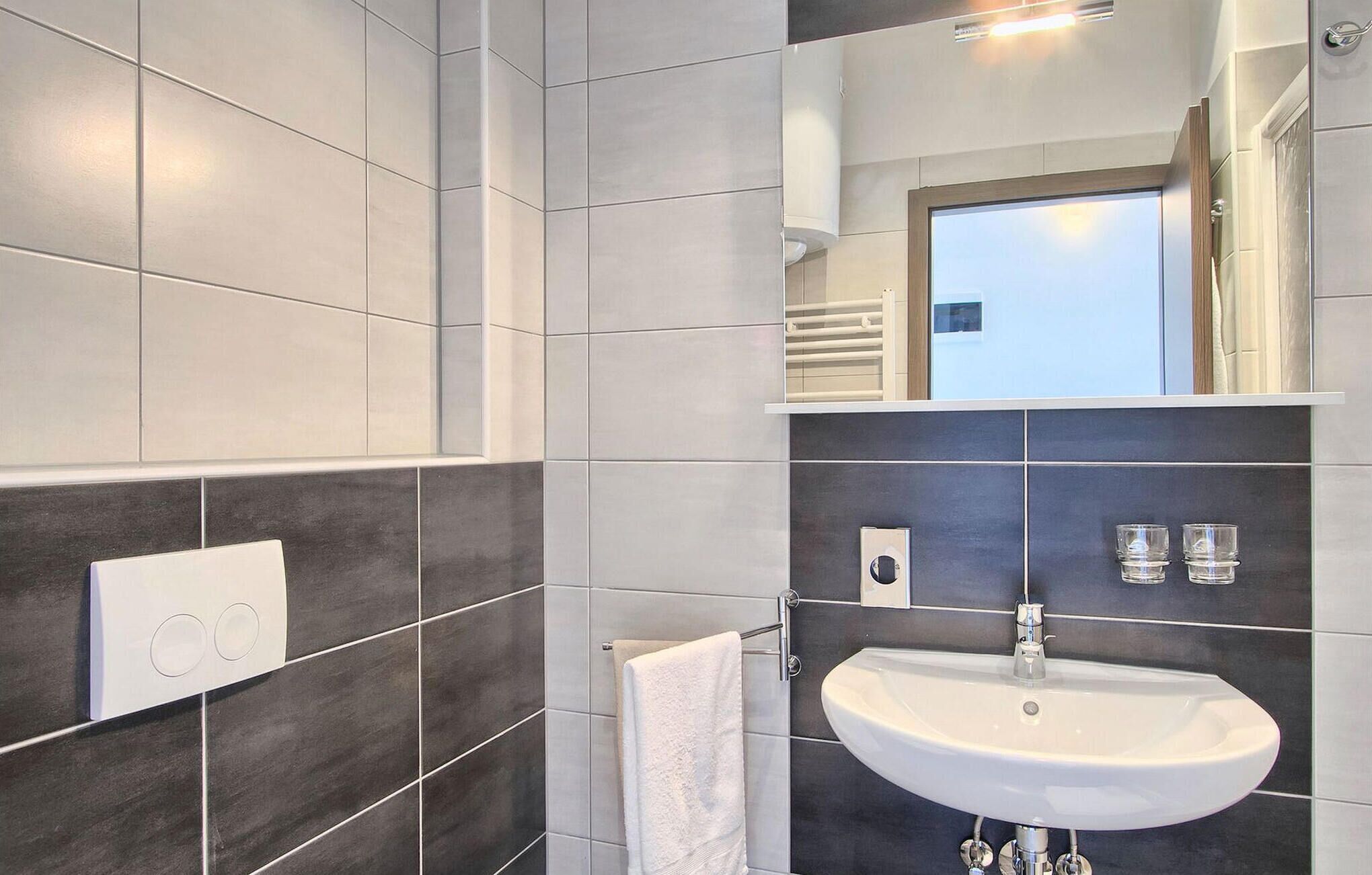 Une salle de bain moderne avec un lavabo blanc, des carreaux foncés, un porte-serviettes et un miroir.