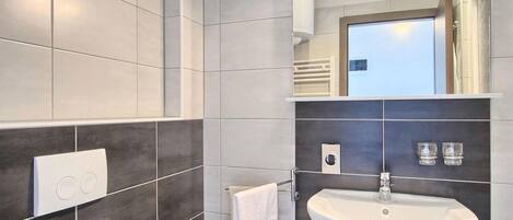 Une salle de bain moderne avec un lavabo blanc, des carreaux foncés, un porte-serviettes et un miroir.