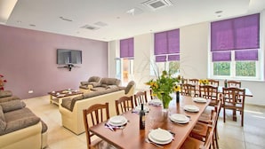 A modern living room with a sofa, dining table set for six, and large windows with purple blinds. - Villa Old School House (Tinjan)