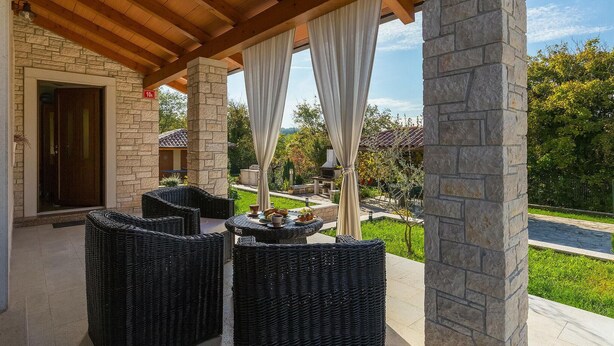 A covered patio area with wicker furniture, stone pillars, and a view of a landscaped garden. - Cozy home in Pazin with WiFi (Pazin)