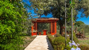 A stone pathway leading to a red pergola with a tiled roof, surrounded by greenery and trees. - Stunning home in Liznjan with sauna (Liznjan)