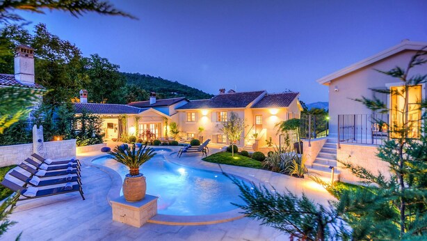Ein luxuriöses Haus mit Pool, Gartenmöbeln und einem gut beleuchteten Garten im Abendlicht.