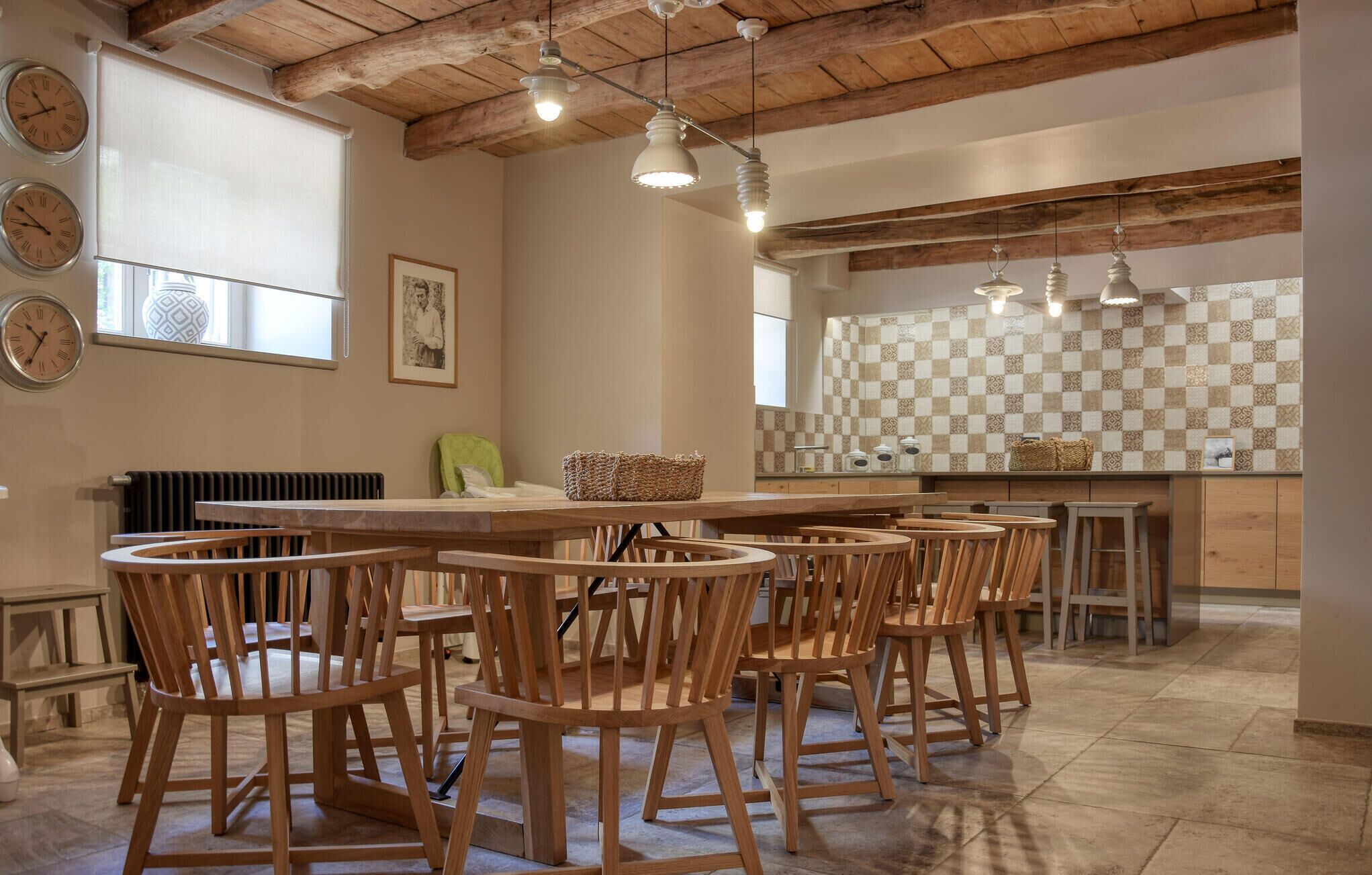 Een ruime eetruimte met houten stoelen en een grote tafel, een keuken met geruit tegels, en een rustiek plafond met zichtbare balken.