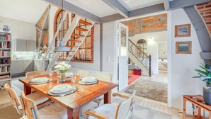 A spacious dining area with a wooden table set for four, surrounded by wicker chairs. A brick wall and a staircase with a metal railing are visible in the background. - Awesome home in Ausacker with WiFi (Ausacker)