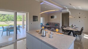 Eine moderne Küche mit Kochinsel, einem Essbereich mit Tisch und Stühlen sowie einem Wohnbereich mit Sofa und Fernseher.