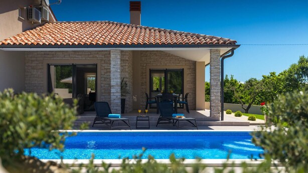 Ein zweistöckiges Haus mit Swimmingpool, Steinfassade und Sitzbereich im Freien.