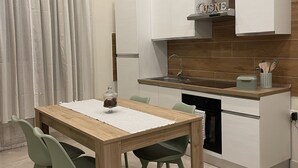 Eine moderne Küche mit weißen Schränken, einer Holzausziehtafel und einem eingebauten Ofen. Ein Esstisch mit Stühlen und ein Fenster mit Vorhängen sind ebenfalls vorhanden.