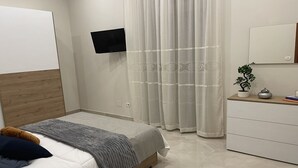 Ein modernes Schlafzimmer mit einem Bett, einem an der Wand montierten Fernseher, einem Schminktisch und einer Zimmerpflanze.