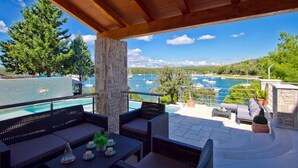 A covered outdoor seating area with wicker furniture, a stone pillar, and a view of boats on a body of water. - Gorgeous home in Pula (Pula)