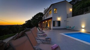 Eine moderne Villa mit Swimmingpool, Sitzgelegenheiten im Freien und Blick auf die umliegende Landschaft.