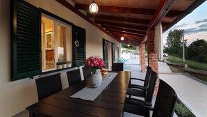 Eine Terrasse im Freien mit einem Holztisch und Stühlen, einer Vase mit Blumen und im Hintergrund ein Blick auf einen Swimmingpool.
