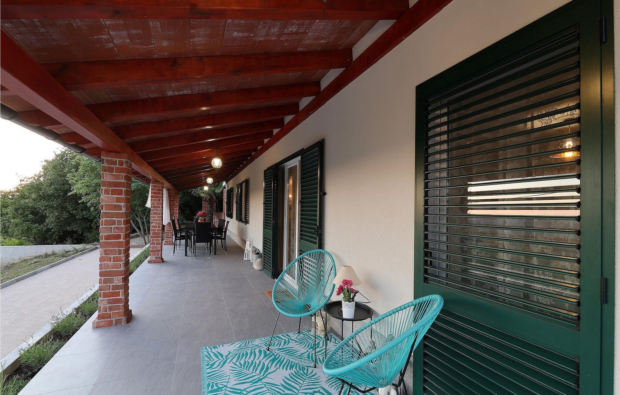 A covered outdoor area with a brick column, a table with chairs, and a window with shutters.