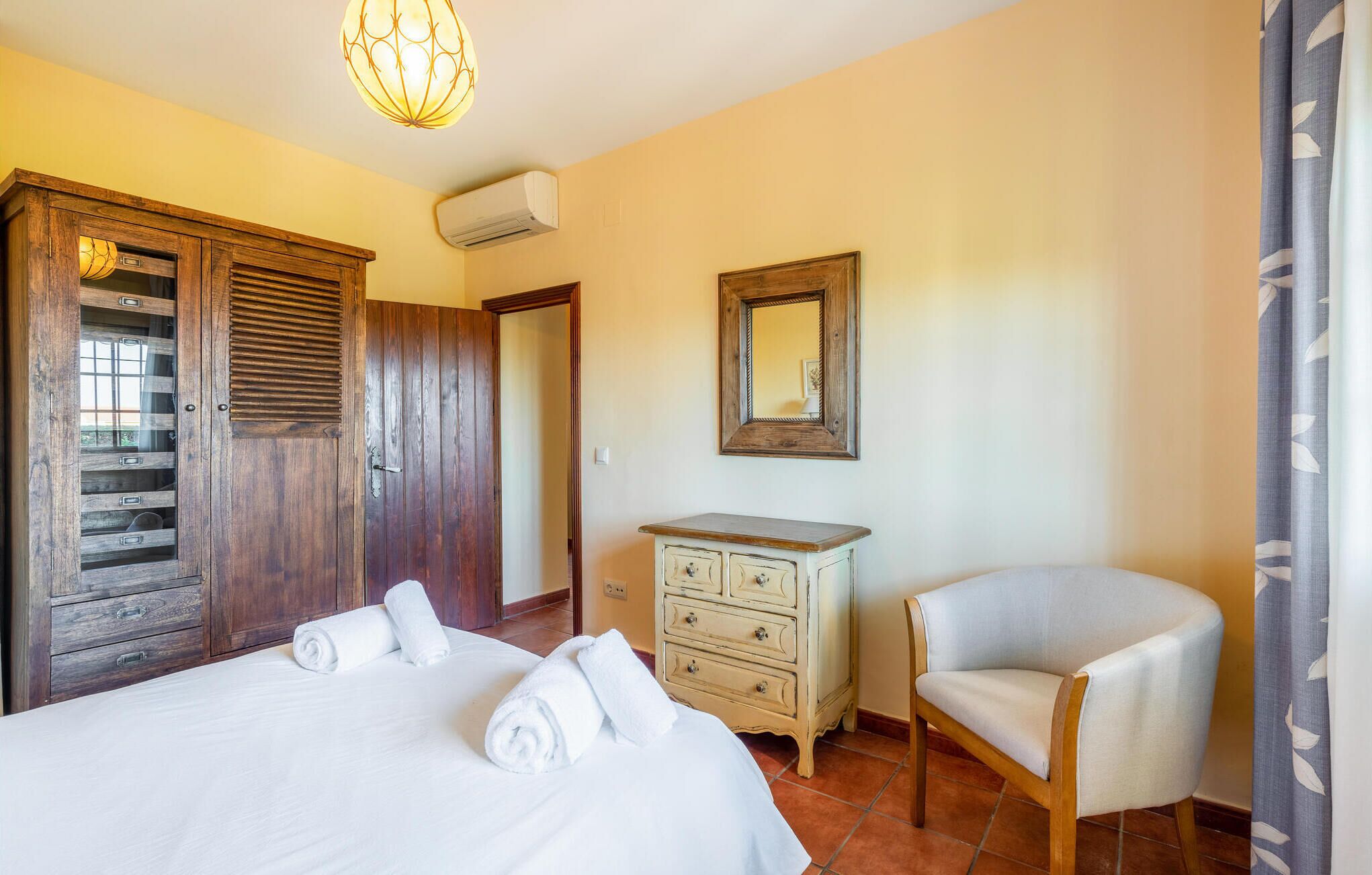 Une chambre avec une armoire en bois, une commode, une chaise et un lit avec des serviettes.