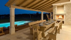 Un espace extérieur aménagé pour les repas, avec une piscine, des meubles en bois et une cheminée en pierre.