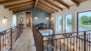 Un intérieur spacieux avec de hauts plafonds, des poutres en bois, un escalier et de grandes fenêtres offrant une vue sur la verdure.