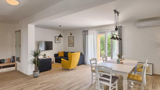 Ett modernt vardagsrum med en soffa, ett matbord med stolar, en tv som är monterad på väggen och ett stort fönster med gardiner.