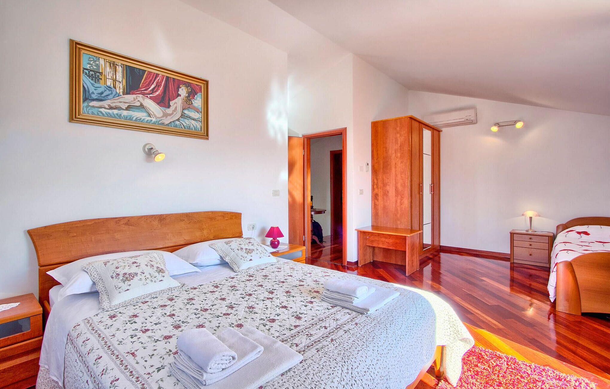 A bedroom with a large bed, a wooden wardrobe, a nightstand, and a painting on the wall.
