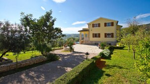 A two-story building with a stone facade, a paved driveway, and a well-maintained garden with trees and shrubs. - Awesome home in Pican (Pican)