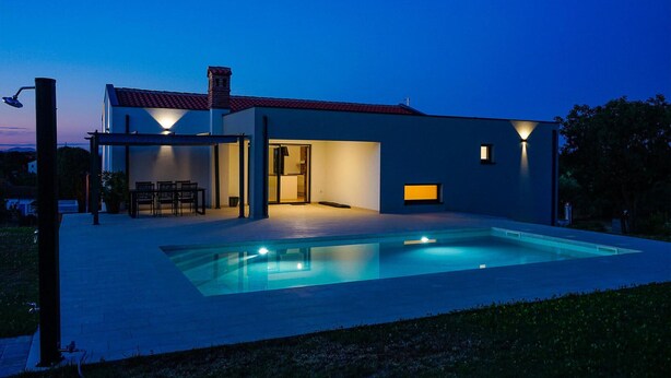 Una casa moderna con piscina, un patio cubierto y una entrada bien iluminada.