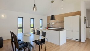 Una cocina moderna con una isla central, armarios blancos y un comedor con mesa y sillas.