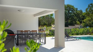 Un patio al aire libre con una mesa y sillas, una parrilla y un área de piscina con sillones de descanso.