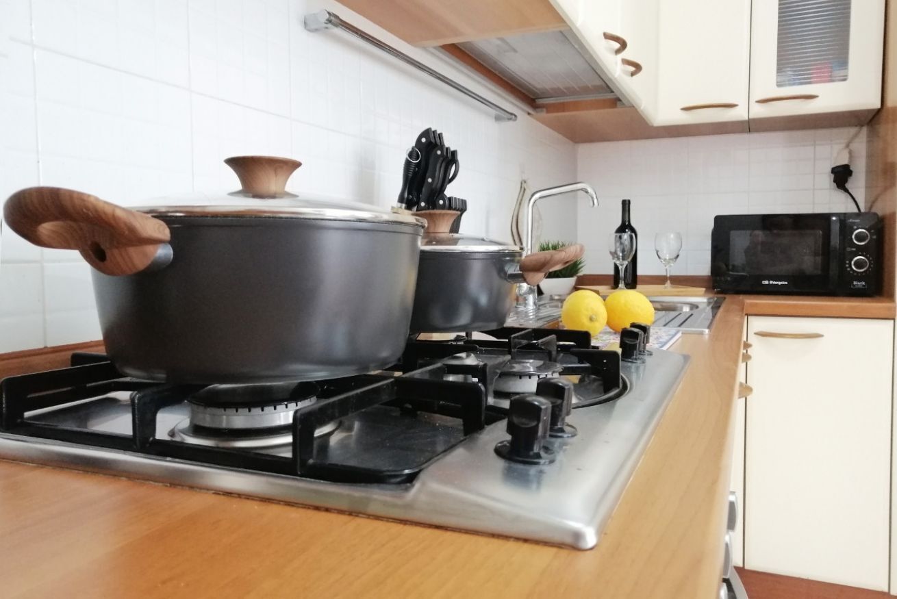 Una cocina con estufa a gas, ollas, microondas y un fregadero.