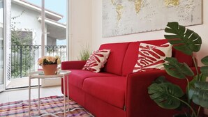 A red sofa with patterned cushions, a small table with a potted plant, and a world map on the wall.