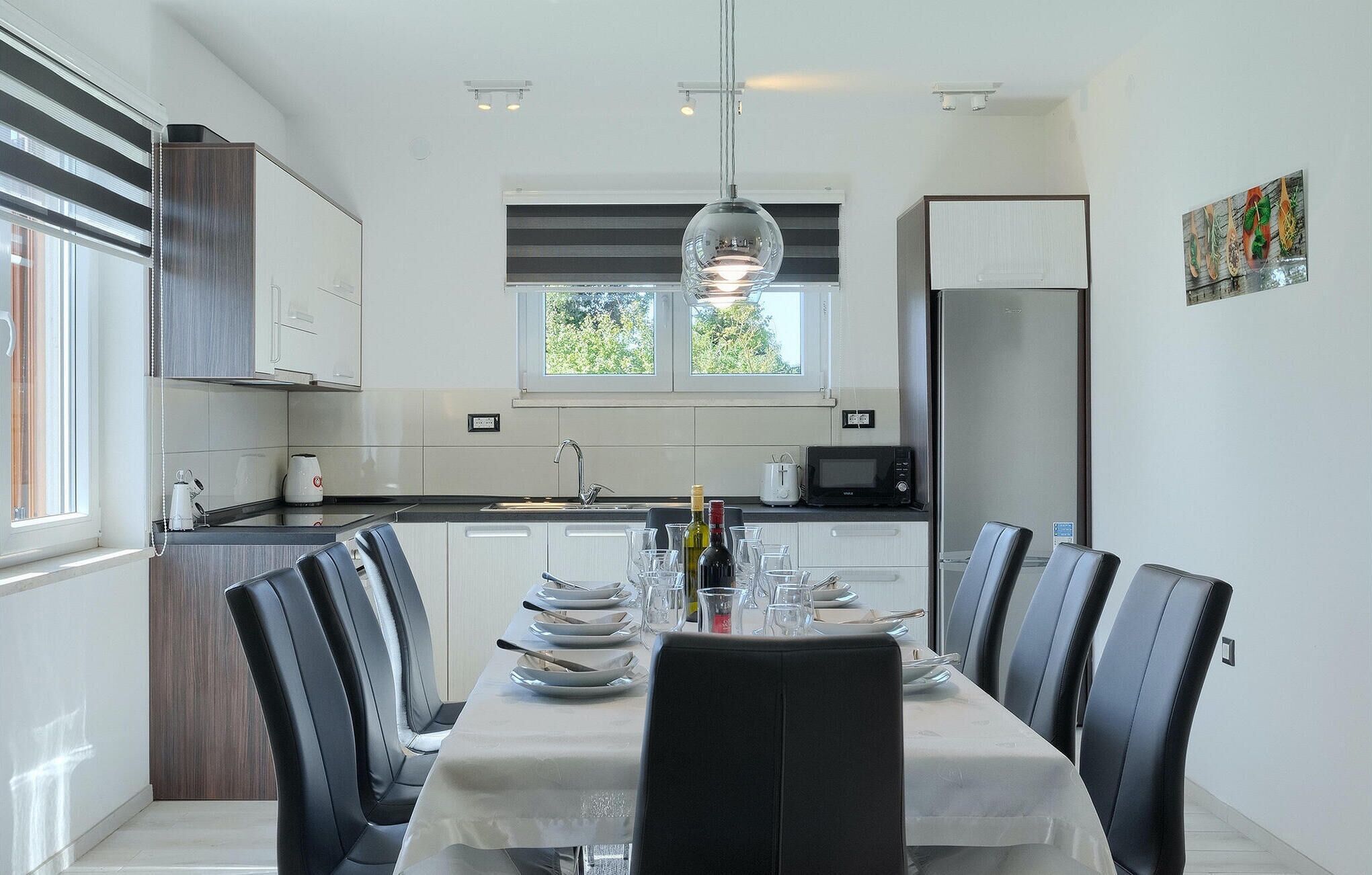 Uma cozinha moderna com armários brancos, uma mesa de jantar posta para seis pessoas e uma janela grande sobre a pia.