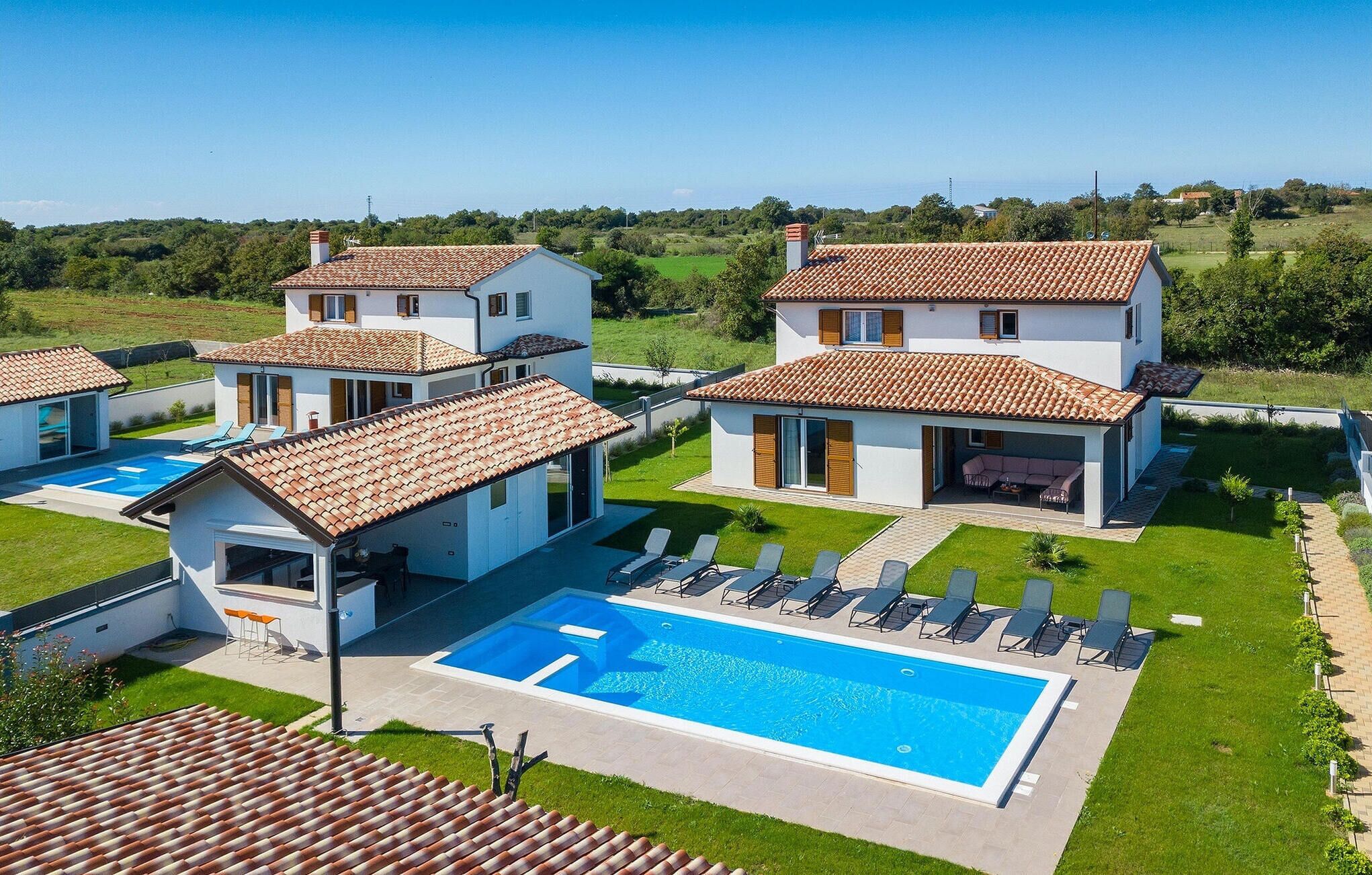 Un complexe résidentiel moderne composé de plusieurs villas, doté d’une piscine et d’une pelouse bien entretenue.