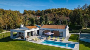 Une maison moderne à deux étages, dotée d’une piscine, d’un espace de détente extérieur et d’une pelouse bien entretenue.
