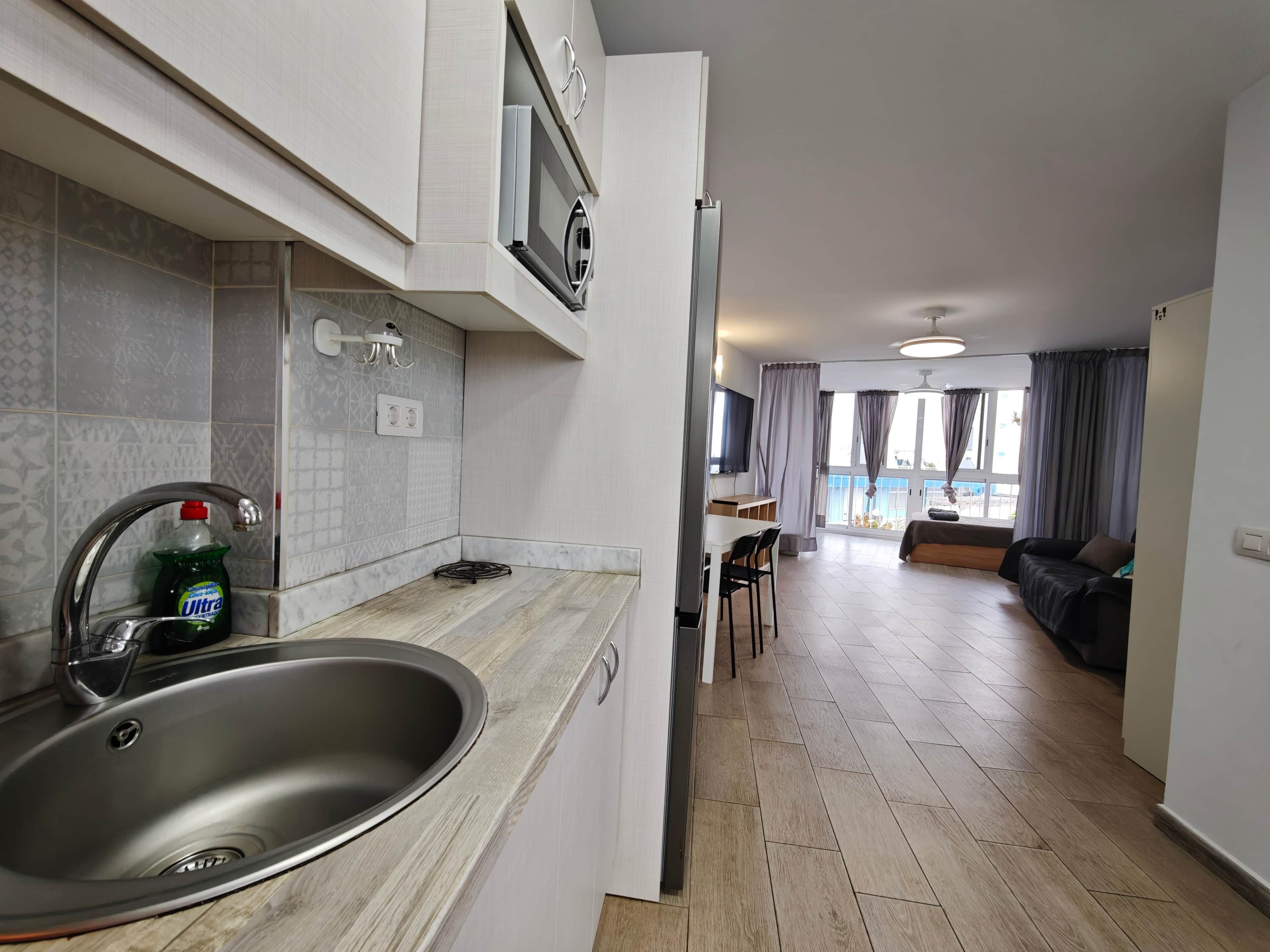 A modern kitchen with a sink, a dining area with a table and chairs, and a living room with a sofa and a TV.