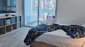 A bedroom with a bed, a TV on a stand, and a balcony with a view of trees. - NEAR THE SEA IN MESA DEL MAR (Mesa del Mar)