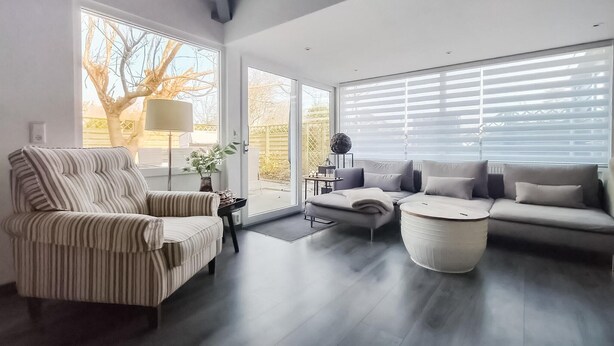 Ein modernes Wohnzimmer mit einem gestreiften Sessel, einem grauen Sofa und einem runden Couchtisch. Große Fenster mit Jalousien, eine Stehlampe und ein dekorativer Globus auf einem Beistelltisch.