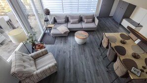 Ein modernes Wohnzimmer mit grauem Sofa, einem gestreiften Sessel, einem runden Couchtisch und einem Essbereich mit Holztisch und Stühlen.
