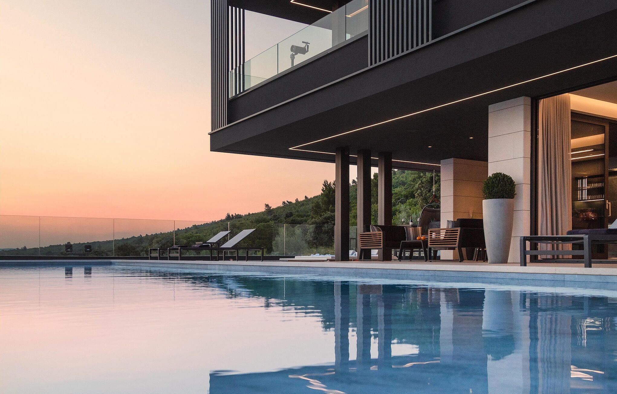Ein moderner Poolbereich im Freien mit freiem Blick auf die umliegende Landschaft und einem Sonnenuntergang.