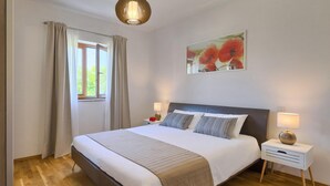 A neatly arranged bedroom with a large bed, two bedside tables, a window with curtains, and a painting above the bed.