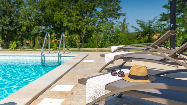 A poolside area with lounge chairs, a hat, and sunglasses on one of the chairs.