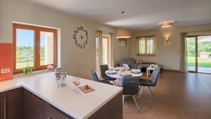 A modern kitchen with a dining area, large windows, and a clock on the wall.