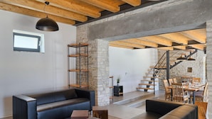 Una sala de estar moderna con un sofá de cuero negro, una mesa de centro de madera y una escalera que lleva a un comedor.