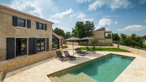Una casa moderna con piscina, paredes de piedra y mobiliario de exterior.