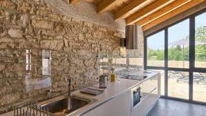 Una cocina moderna con paredes de piedra, un lavamanos de acero inoxidable y un amplio ventanal con vistas a un patio.
