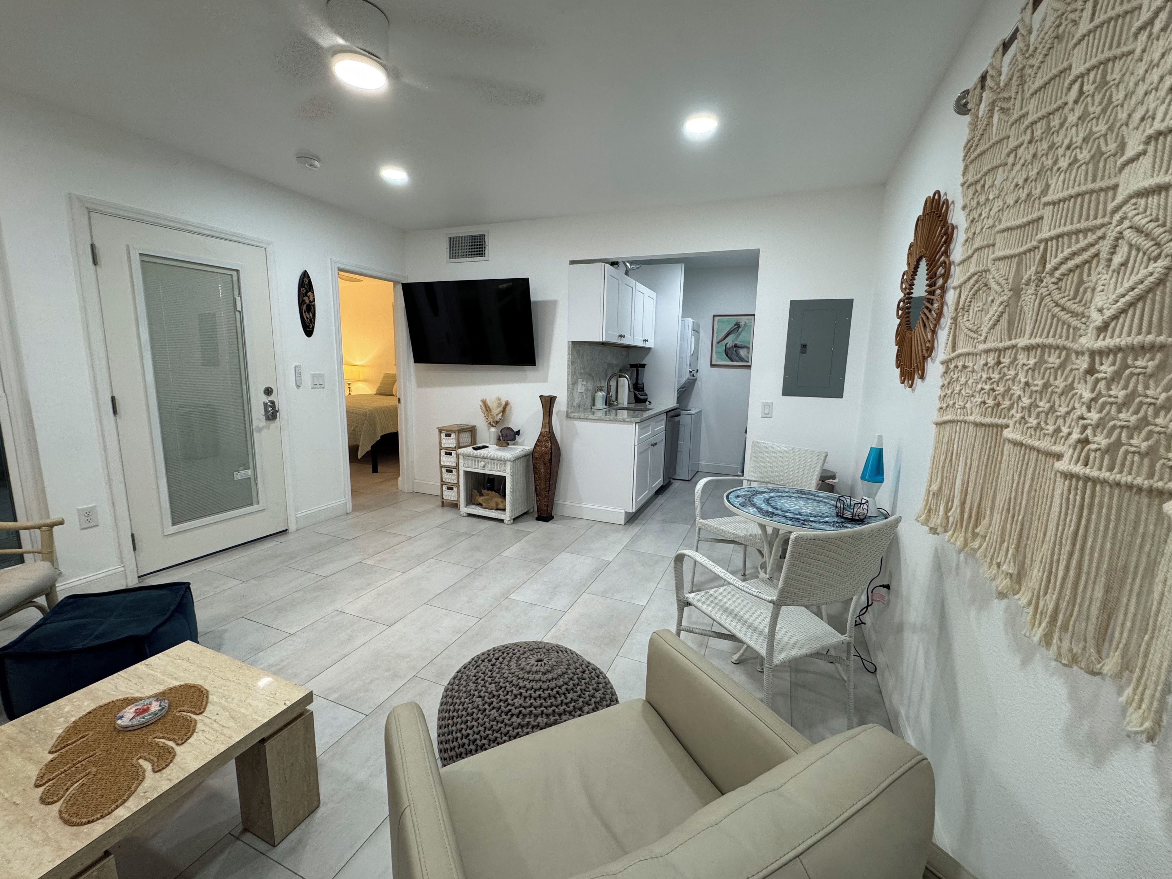 A modern living room with a sofa, a coffee table, and a TV. There is a kitchen area with cabinets and a dining table.