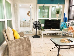 A living room with a TV, fan, wicker furniture, and a glass coffee table.