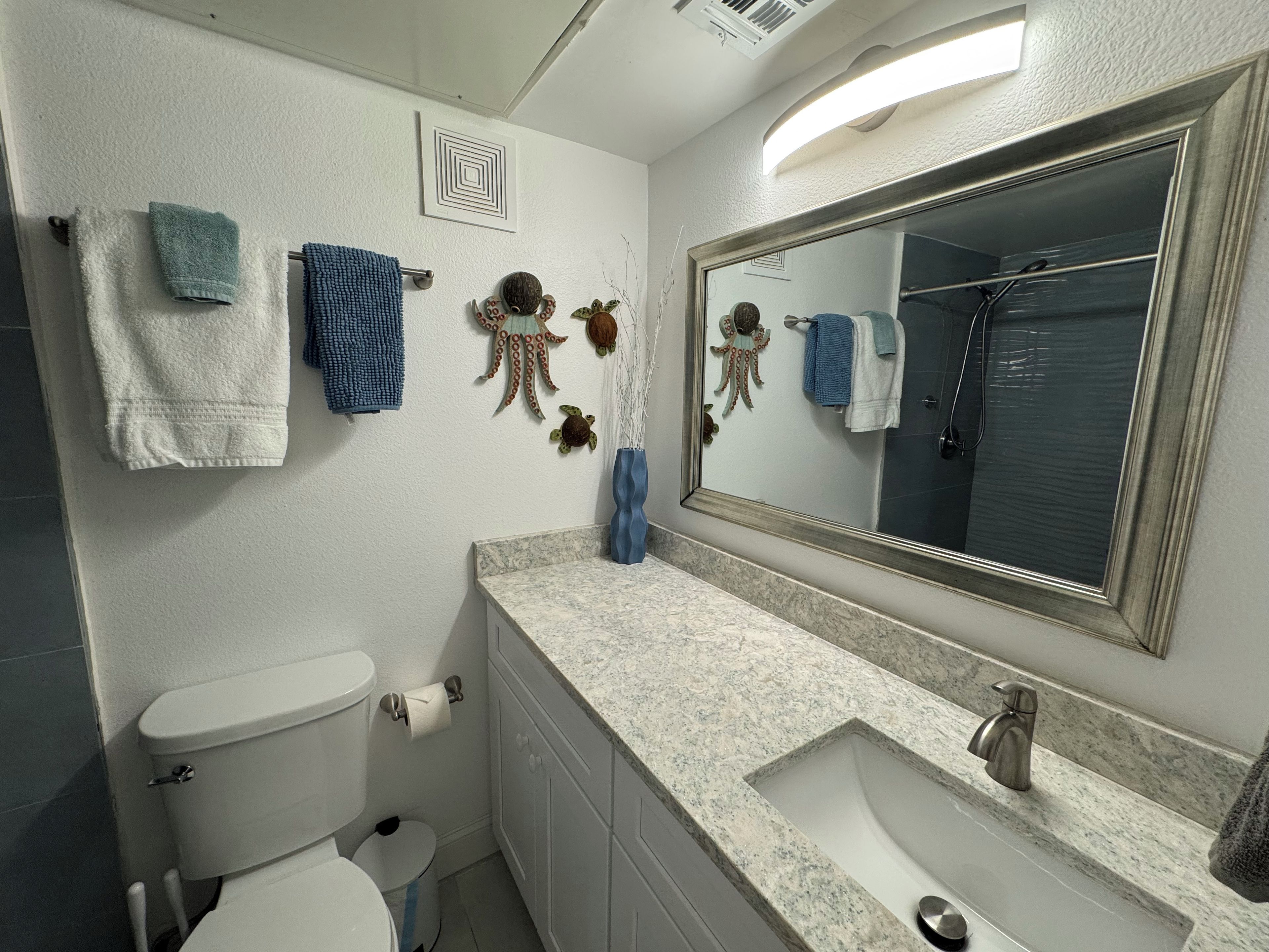 Un baño con inodoro, lavamanos y espejo. Hay toallas colgadas en la pared y una decoración de pulpo ornamental.