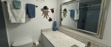 Un baño con inodoro, lavamanos y espejo. Hay toallas colgadas en la pared y una decoración de pulpo ornamental.