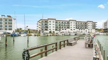 A marina with docked boats, a wooden pier, and a large hotel building in the background.