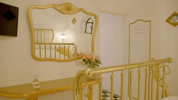 A room with a large ornate mirror, a small bedside table with a bottle, a flower arrangement, and a sign reading "PROHIBITED FLAMING".