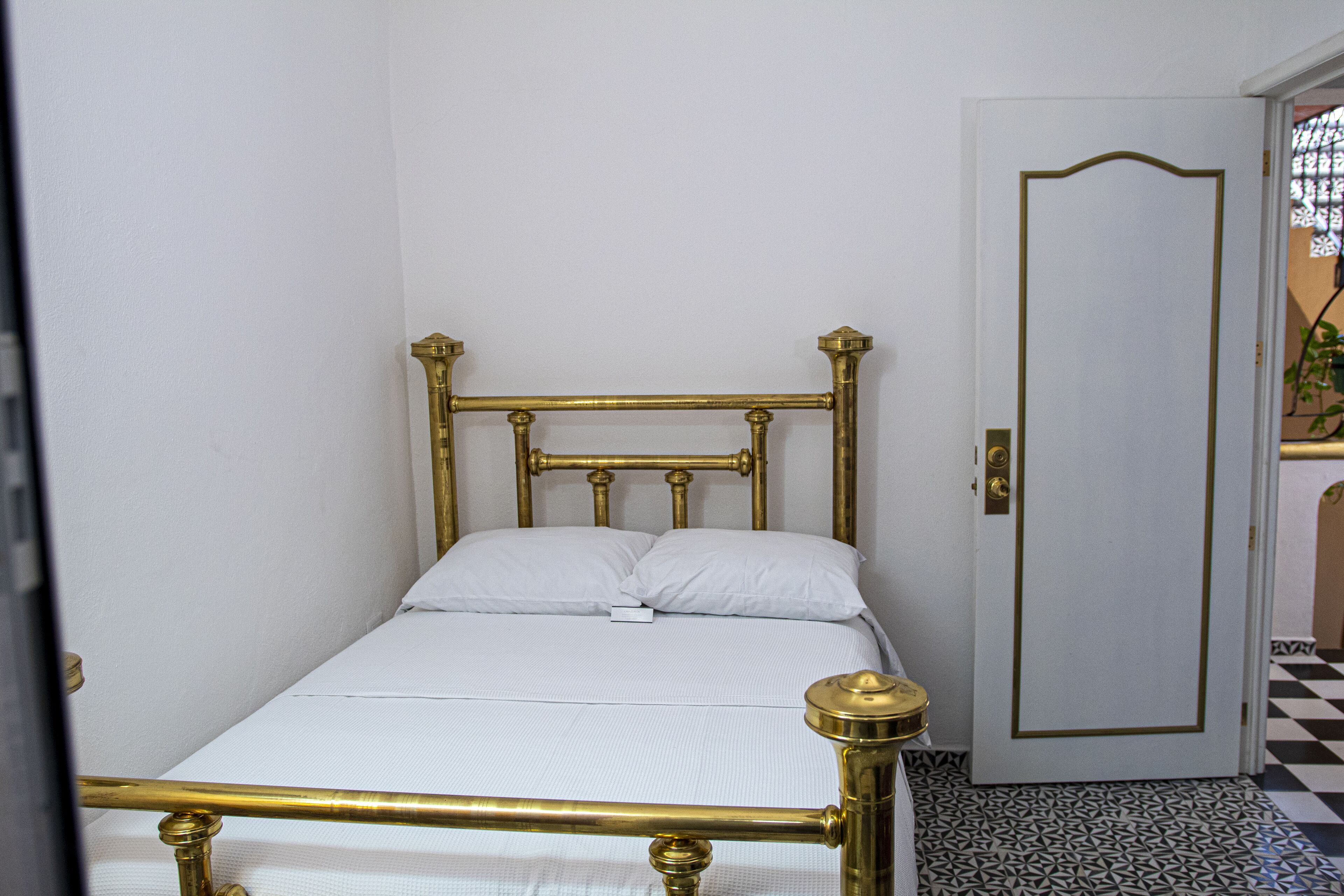 A single bed with a gold frame and white bedding in a room with a checkered floor pattern.